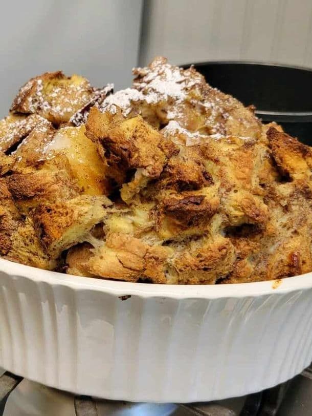 A baked bread pudding topped with powdered sugar in a white dish.