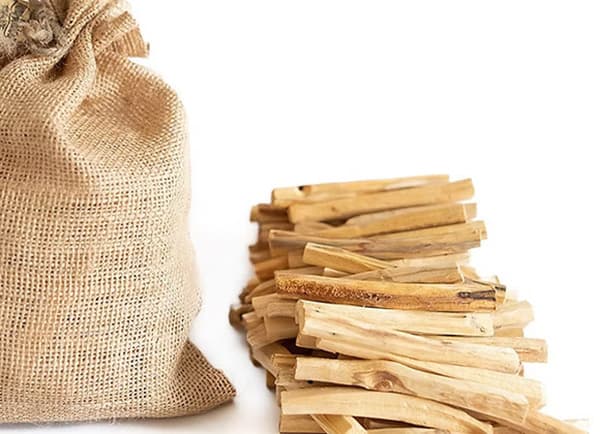 A burlap sack beside a pile of wooden sticks.