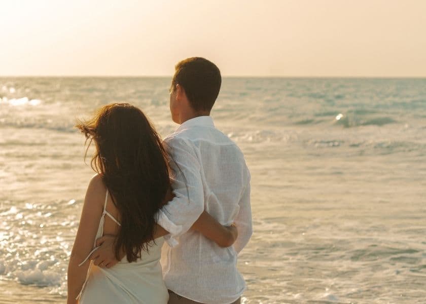 A couple stands together on the beach, gazing at the ocean during sunset. A couple stands together on the beach, gazing at the ocean during sunset.