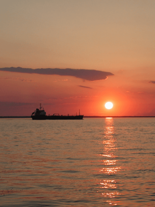 A silhouetted ship sails on calm waters beneath a vibrant sunset.