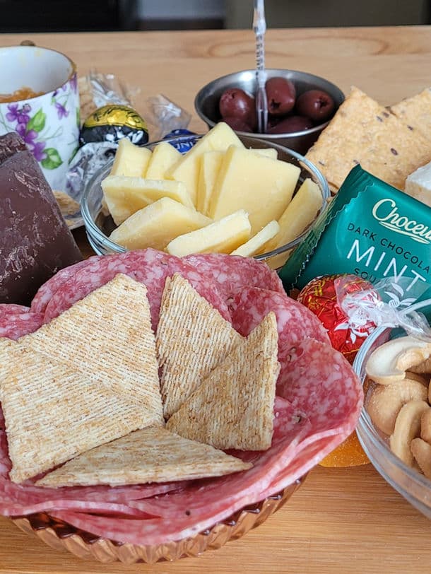 A colorful spread of cheeses, meats, crackers, chocolates, nuts, and olives arranged on a wooden table.
