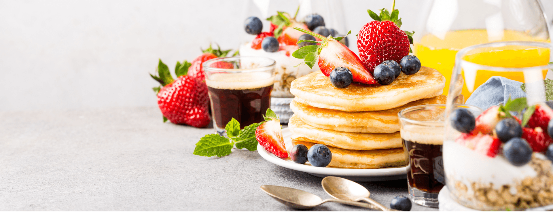A stack of pancakes topped with strawberries and blueberries, accompanied by coffee, yogurt, and orange juice.
