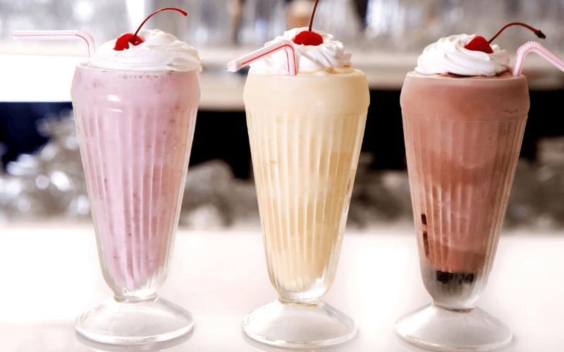 Three colorful milkshakes topped with whipped cream and cherries, served in tall glasses.