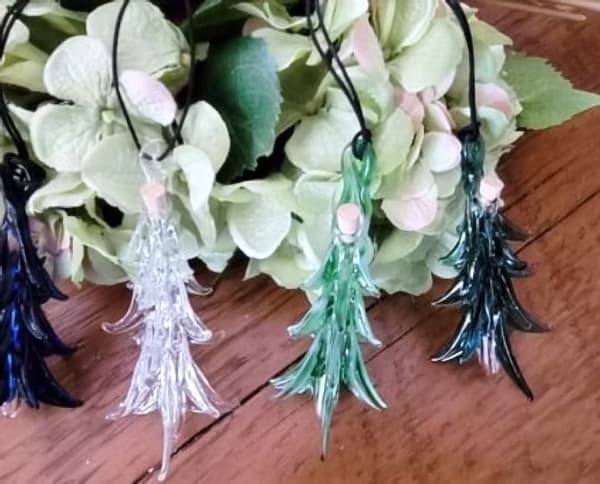 Four decorative glass tree pendants in shades of blue, green, and clear, arranged next to green foliage.