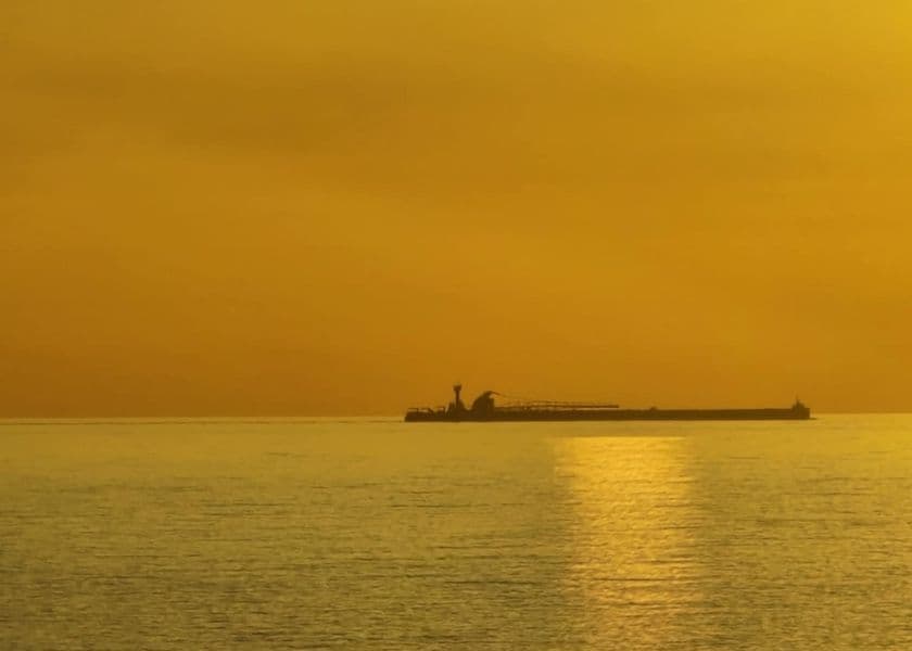 A freighter on Lake Huron at sunrise, surrounded by a surreal golden sky and glow.